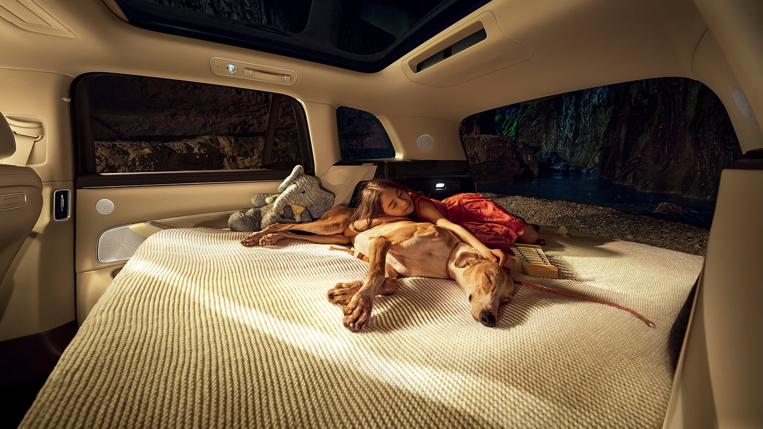 一个小女孩抱着一只狗躺在问界 M8 白沙杏展开的大床上睡觉